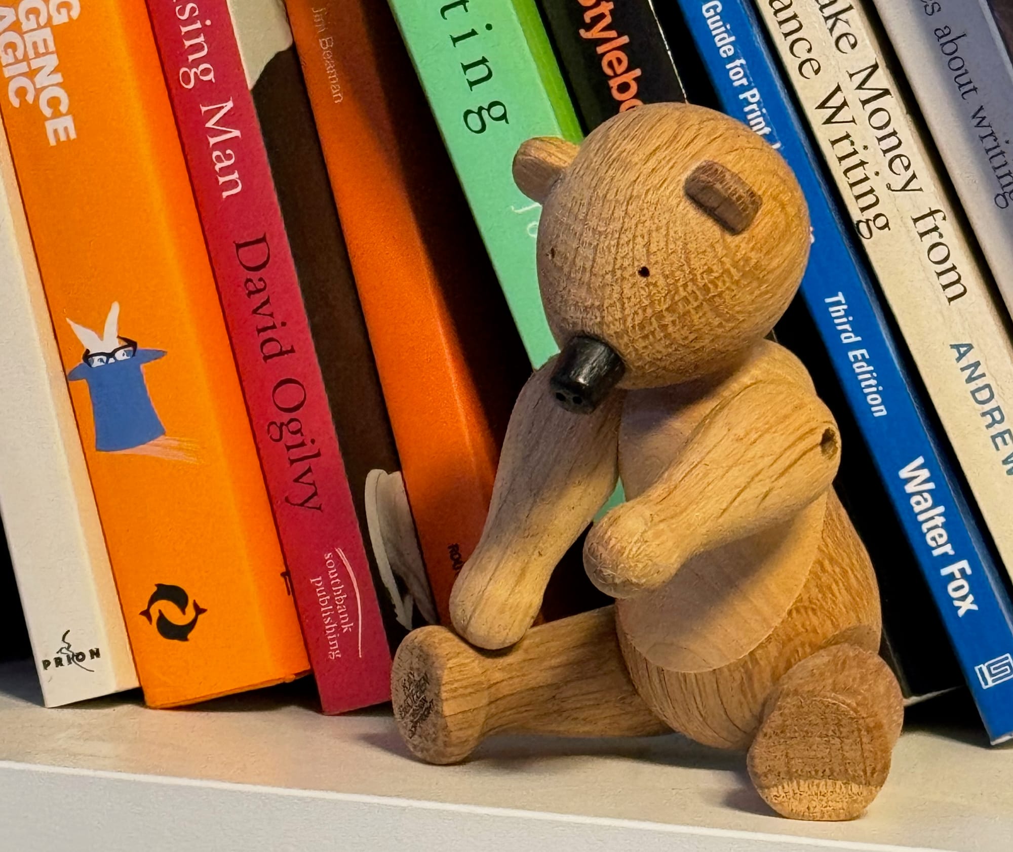 A small wooden bear on a shelf full of books. 